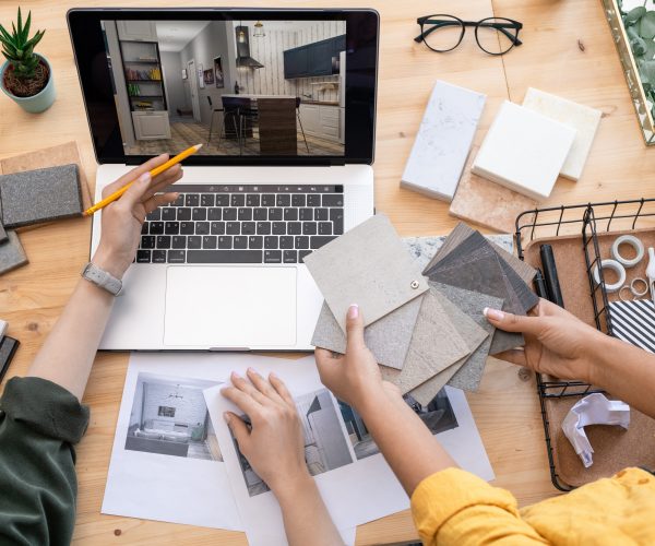 Contemporary designer pointing at home interior example on laptop display while consulting with colleague holding linoleum samples